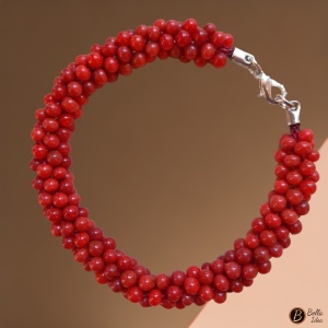 Braccialetto Kumihimo in perline rosse di vetro lumè  con chiusura argentata su sfondo rosa.