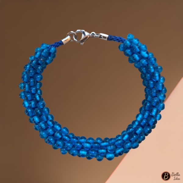 Braccialetto Kumihimo in perline blue di vetro lumè  con chiusura in acciaio su sfondo rosa.