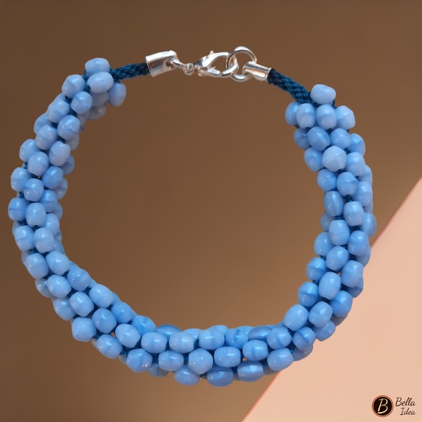 Braccialetto Kumihimo in perline ovaline azzurre di vetro lumè con chiusura argentata su sfondo rosa.
