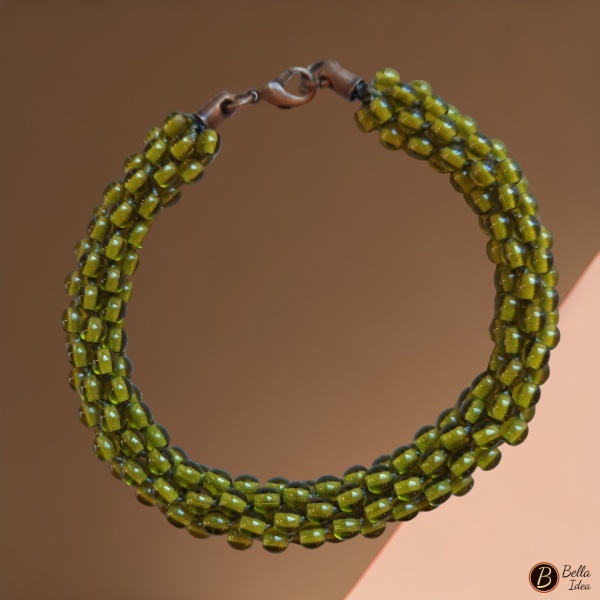 Braccialetto Kumihimo in perline verde oliva di vetro lumè  con moschettone ramato su sfondo rosa.