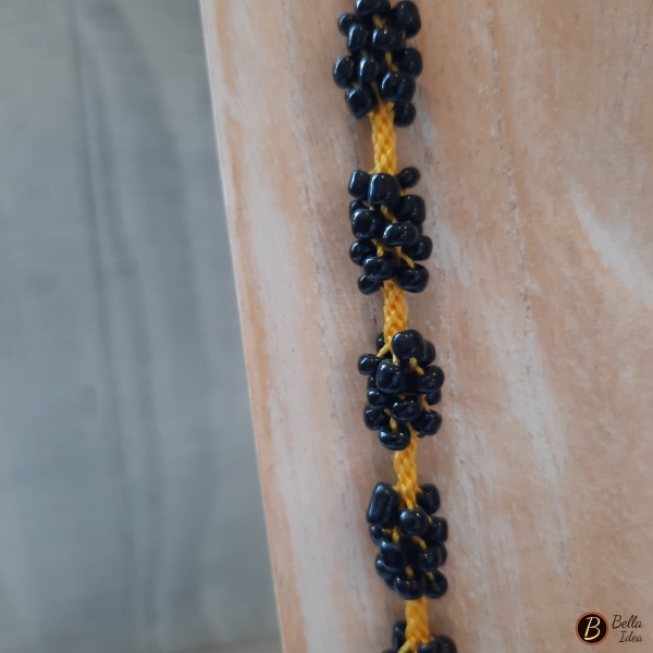 Dettaglio di collana Kumihimo in perline tonde nere intercalata a filo giallo con chiusura dorata.