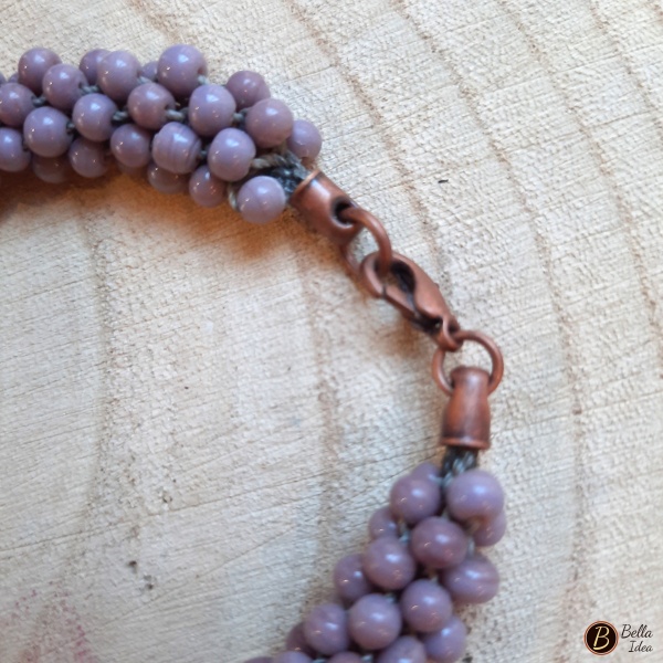 Dettaglio di braccialetto Kumihimo in perline color glicine di vetro lumè con chiusura ramata.