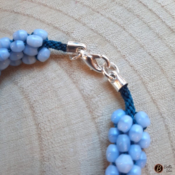 Dettaglio di braccialetto Kumihimo in perline ovaline azzurre di vetro lumè con chiusura argentata.
