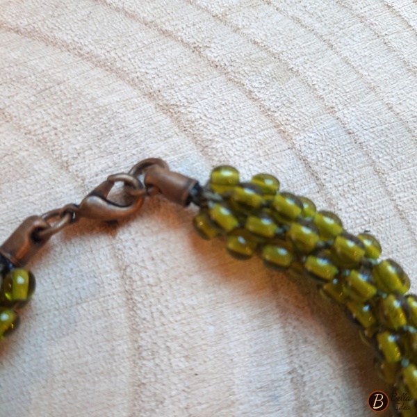 Dettaglio di braccialetto Kumihimo in perline verde oliva di vetro lumè  con moschettone ramato.